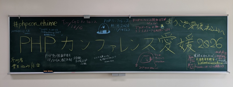 黒板に次の文字が書かれている。中央に大きく「PHP カンファレンス愛媛 2026」。周りに「#phpcon_ehime」「ようこそ愛媛松山へ」「参加者書き込み自由」「みかんおいしいよ Larao」「2027.3.20-22 PHPerKaigi 2027 #PHPerKaigi」「TinyGO カンファレンス 10/10」「PHP カンファレンス新潟 2026 11/14 (土)」「PHP カンファレンス関西@京都 1/16 (土) プロポーザルお願い リクエストークもお願いします！」「PHP 勉強会@東京 10/21 (水) 配信有!!」「えひめたのしい！ ことみん」「エヒメ出身だけど札幌からきました!! Shima-kou」「2027.04.10 おだわらーー! えひめさいこー!! asumikam」「覚悟がキマッたので北海道富良野市で TechRAMEN 2026 Conference やります →40分ハンズオンをたくさん募集します 旭川空港からがいいです 富良野駅近くの宿がいいです (テックラーメンで宿いくつかおさえてます) 11/20 (金) 17:00 くらい start → 11/21 (土) 9:30 くらい start」